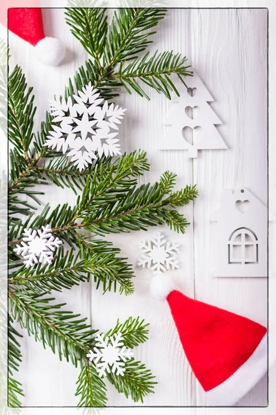 Composição de Natal em um fundo branco. Ramos de árvore de Natal, chapéu de Papai Noel, flocos de neve decorativos e uma pequena casa. Vista superior — Fotografia de Stock