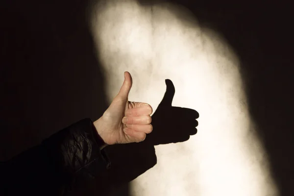 Woman hand thump up sign and shadow on a wall