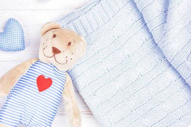 Kırmızı kalbi ve bebek mavisi örgü ören sevimli bir oyuncak ayı.