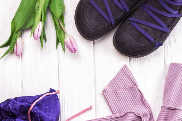 Stylish shoes, clothes and spring flowers tulips on a white wooden background. Flat lay shot of girls spring clothing