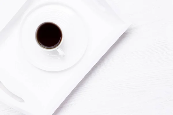 White cup of black coffee on a white wooden background. New life chapter concept. Top view, copy space
