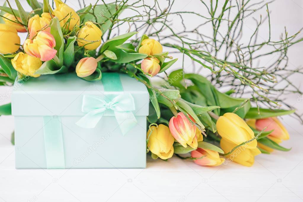 Delicate elegant gift box and a lot of spring yellow tulips on a white background