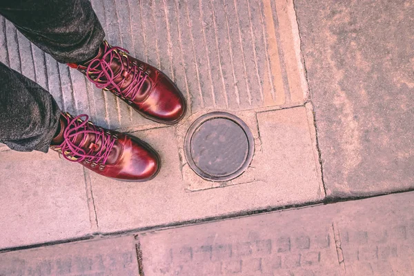 Las botas a la moda de color burdeos en el pavimento de la ciudad y bolardo metálico eléctrico bajo tierra. Pilona retráctil — Foto de Stock