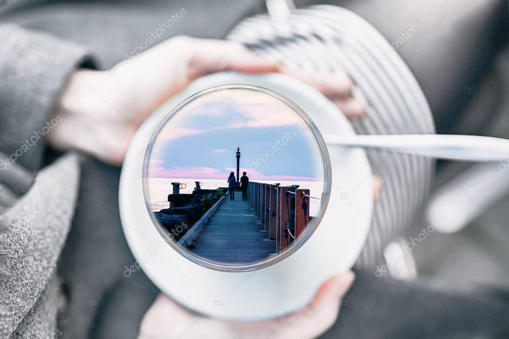 Female hands holding a cup with couple in love inside. Concept of romantic memory. Gray day, colorful dreams