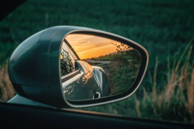 Bir arabanın yan aynasında güzel gün batımı. Yeşil doğa arka planı
