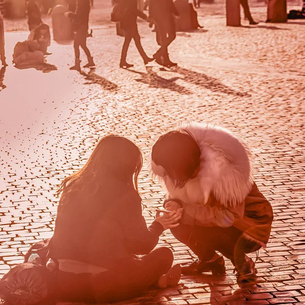 Två tjej vänner sitter på trottoaren och tittar på en av sina smartphones. Korall färgtonas foto — Stockfoto