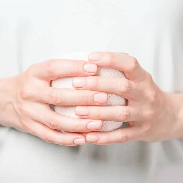 Hermosas manos femeninas sosteniendo copa blanca. Manicura con esmalte de uñas desnudo . — Foto de Stock