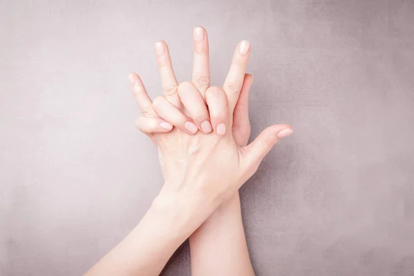 Hermosas manos femeninas sobre un fondo gris. Manicura con esmalte de uñas desnudo. Concepto de cuidado de manicura. Copiar espacio — Foto de Stock