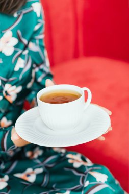 Kadın elleri kırmızı bir kanepe arka plan üzerinde çay beyaz fincan tutan. Kopyalama alanı