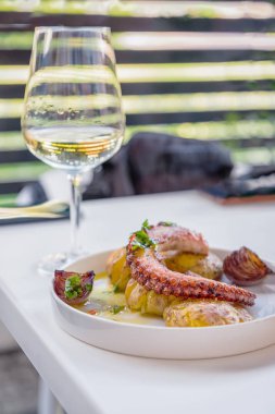 Beyaz tabakta ızgara ahtapot, fırında patates ve çizgili bir arka plan üzerinde beyaz şarap bir bardak. Geleneksel Portekiz yemeği. Deniz ürünleri