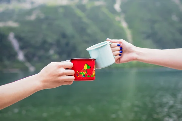 Manos femeninas tostadas con tazas de ancho. Menta y tazas rojas en el fondo de la naturaleza. Parque Nacional Tatra, Polonia. Famoso lago Morskie Oko — Foto de Stock