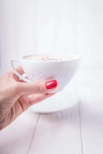 Женская рука держит белый фарфор чашку кофе капучино с корицей. Маникюр с красным лаком для ногтей. Копирование пространства — стоковое фото