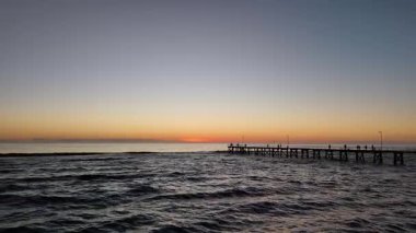 Güney Adelaide, Güney Avustralya 'daki Port Noarlunga Sahili' nin nefes kesici 4K hava aracı görüntüleri. İskele, resif, kıyı şeridi ve turkuaz okyanus suları üzerinde altın gün batımı manzarası. Güney Avustralya 'nın çarpıcı bir sahil kaçışı doğal güzelliğini gözler önüne seriyor.