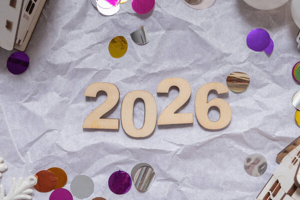 Декоративные элементы окружают 2026 год, демонстрируя праздничную атмосферу, наполненную яркими красками. Мерцающие конфетти добавляют волнения, когда люди готовятся к празднованию.