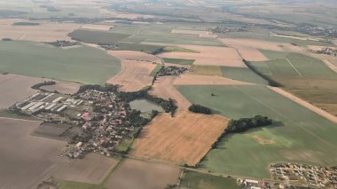 Çarpıcı bir hava görüntüsü, pitoresk bir kırsal bölgedeki tuhaf bir köyün yanındaki canlı tarlaları gösteriyor.