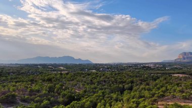Nefes kesici ve çarpıcı yeşil bir manzara. Uzak, görkemli dağları barındıran parlak mavi bir gökyüzü altında.