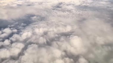 Bir uçak penceresinden mükemmel çerçevelenmiş yumuşak ve kabarık beyaz bulutları gösteren nefes kesici hava görüntüleri