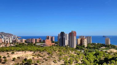 Parlak mavi gökyüzünün altındaki yemyeşil araziye uyum içinde deniz kenarındaki binaların çarpıcı manzarası.