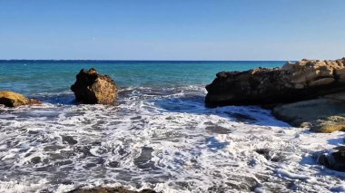 Çarpıcı bir panoramik okyanus manzarası dalgalar engebeli kayalık bir sahile çarpıyor berrak mavi gökyüzünün altında