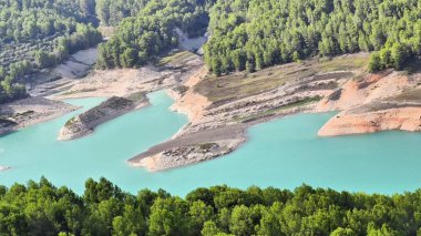 Sersemletici hava manzarası, canlı ve gür yeşilliklerle çevrili sakin bir göl sergiliyor.