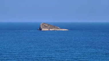 Sakin mavi okyanus sularıyla çevrili kayalık bir adanın nefes kesici ve çarpıcı manzarasını deneyimleyin.