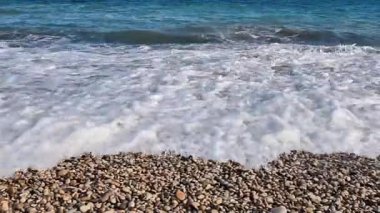 Sakin bir sahil sahnesinde yumuşak dalgalar berrak bir gökyüzünün altında durmaksızın yuvarlanır.