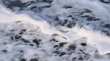 Bu sahne, güçlü dalgaların çakıllı bir sahile çarptığını ve doğanın çarpıcı güzelliğini ortaya çıkardığını gösteriyor.