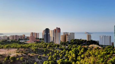 Canlı bir sahil şehrinin nefes kesici manzarası modern gökdelenlerle bezenmiş yemyeşil yeşilliklerin yanında.
