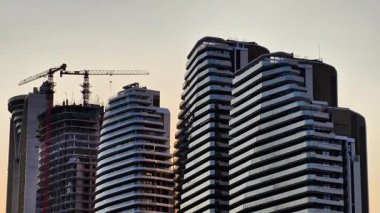 Günbatımında hareketli bir inşaat alanının yanında kentsel gökdelenleri gösteren çarpıcı ve dramatik bir manzara