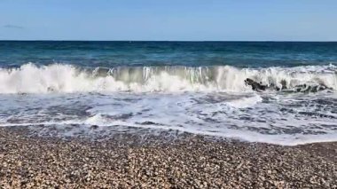 Sakin dalgaların rahatlatıcı sesini hisset. Açık mavi gökyüzünün altındaki güzel bir çakıl taşı plajına hafifçe dokun.