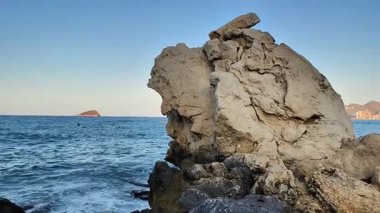 Huzurlu denizin yanında çarpıcı bir kaya oluşumu, doğanın güzelliğini ve sükunetini gözler önüne seriyor.