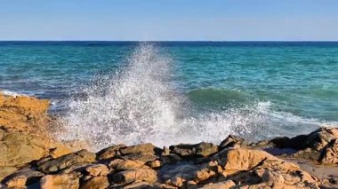 Dinamik okyanus dalgaları, parlak açık gökyüzü ve güneşli plajlar doğal güzelliklerle dolu canlı bir sahil manzarası yaratır.