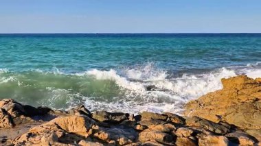 Okyanus dalgalarının, berrak mavi gökyüzünün altındaki engebeli kayalara çarpması nefes kesici bir şekilde büyüleyici bir manzara.
