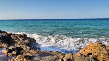 A stunningly beautiful ocean view showcases crashing waves dancing against rugged rocks beneath a clear blue sky