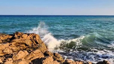 A beautifully serene view of ocean waves gently interacting with rugged rocks beneath a clear blue sky