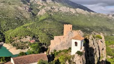 Bir hava görüntüsü, doğadaki canlı yeşil dağların arasına kurulmuş tarihi bir şatoyu güzel bir şekilde yakalar.
