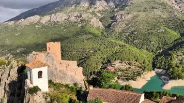 Huzurlu bir göl kenarındaki tarihi bir şatonun çarpıcı manzarası, bereketli dağlarla çevrili, cazibesini artırıyor.