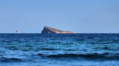 A beautiful, isolated island rises from the serene ocean, featuring tranquil waters, lush greenery, and a clear sky