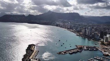 An impressive aerial view of a vibrant coastal city with a lively marina and stunning mountains in the background