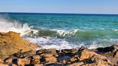 Experience the soothing rhythm of ocean waves crashing against rugged rocks in a peaceful coastal scene