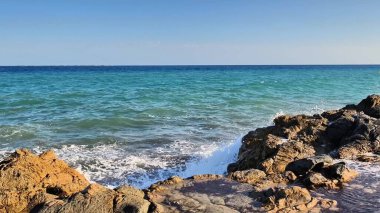 A stunningly beautiful seaside view showcasing brilliant turquoise water crashing against rugged rocky outcrops