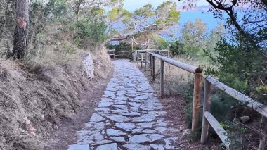 Güzelce işlenmiş taş bir patika zarif bir şekilde yemyeşil tarafından çevrelenmiş ve kıyı şeridinin çarpıcı bir manzarasına yol açıyor.