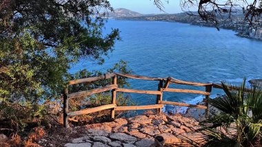 Resimli kıyı şeridinde ağaçlı kayalıklar ve etkileyici bir şehir manzarası var. Kaçış için heyecan yaratıyor.