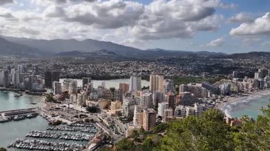 Canlı bir sahil şehrinin havadan görünüşü. Arkasında hareketli bir marina ve çarpıcı dağlar var.