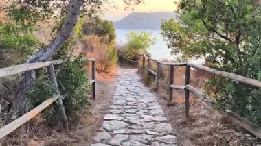 Bereketli bitki örtüsü tarafından çerçevelenmiş, sakin sulara ve manzaralı tepelere doğru yol gösteren pitoresk bir taş patika..