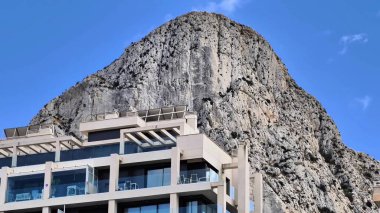 A breathtaking view of a rocky mountain towering over a sleek modern building under a clear blue sky