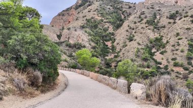 A beautiful and picturesque winding road is surrounded by lush greenery and rugged, majestic hills nearby