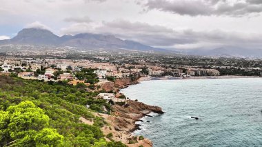 Stunning coastal landscape featuring mountains, rocky shoreline, and a serene sea under cloudy skies.
