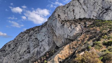 A breathtaking and stunning view of a rocky cliff that is richly detailed against a vibrant blue sky filled with clouds