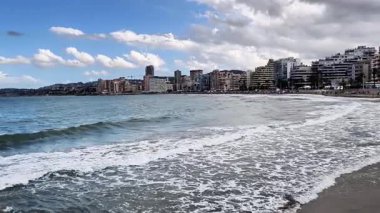 Güzel bir sahil manzarası okyanusun yanında yaşayan şehir sakinlerini gösteriyor. Hafif dalgalar ve bulutlu bir gökyüzü..